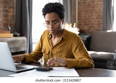 Focused millennial Black business woman calculating finance, money, using calculator, laptop computer at home workplace table, counting budget, paying bills, taxes, rent, mortgage fees