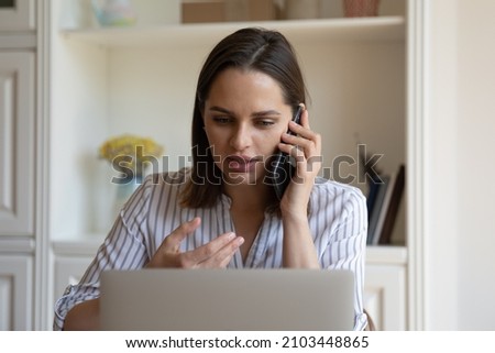 Focused millennial business professional woman talking to client on mobile phone, making telephone call from office workplace, negotiating on project, consulting work app on laptop computer