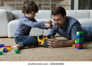 Focused millennial dad and little son repairing toy car with screwdriver, playing learning games on heating floor. Father and kid enjoying playtime together, enjoying leisure time at home