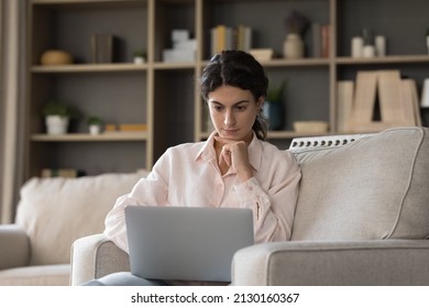Focused millennial generation Hispanic woman looking at laptop screen, reading media news, web surfing, considering problem solution working on online project or doing difficult alone at home. - Shutterstock ID 2130160367