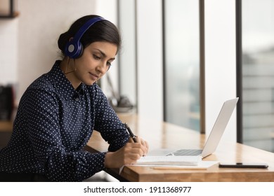 Focused Millennial Indian Woman Interpreter Write Translation From Foreign Language To English Listen To Audio Record In Headset. Attentive Hindu Female Trainee Hearing Lecture Course Online Take Note