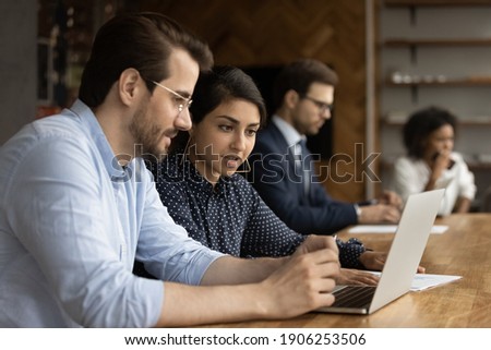 Focused millennial male intern look at laptop screen listen to skilled indian female mentor. Hindu woman experienced worker consult young man new employee help in computer work at corporate network ストックフォト © 