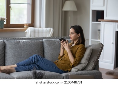 Focused millennial professional woman having mobile phone call on speaker, recording audio message for online chat on cellphone resting on couch. Business woman using voice recognition app on cell - Powered by Shutterstock