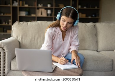 Focused millennial student girl in big wireless headphones writing down online class notes, watching learning webinar, workshop on laptop computer, sitting on couch, studying on internet at home - Shutterstock ID 2093630671