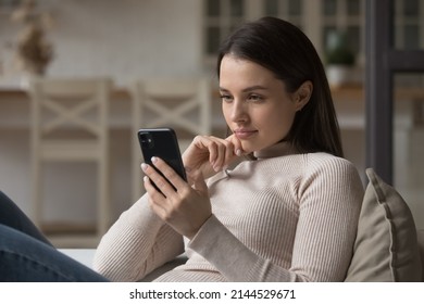 Focused millennial woman using mobile phone at home, reading online content, browsing internet, shopping with application. Gen Z girl texting message on chat on cellphone at home - Shutterstock ID 2144529671
