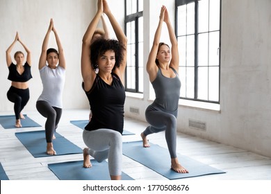 Focused mixed race young girls standing in virabhadrasana 1 pose, strengthening muscles or training endurance together in warrior 1 position barefoot on yoga sport mat at group lesson in studio. - Powered by Shutterstock