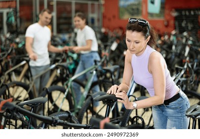 Focused modern woman testing and assessing saddle while choosing bicycle in store, looking for comfort and fit for cycling activities - Powered by Shutterstock