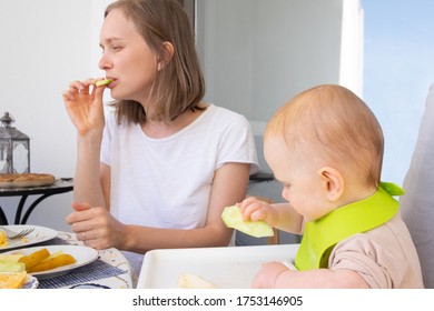 Focused Mom And Baby Daughter Eating Fresh Vegs Together. First Solid Food Or Child Care At Home Concept