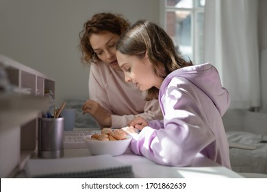 Focused Mom Helping Teenage Daughter Doing Homework Studying From Home. Young Adult Parent Mum Or Tutor, Coach Teaching School Child, Explaining Distance Learning Education Reading Book Together.