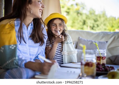 Focused Mother And Daughter Looking Paper Schedule Notebook Together Relaxing At Outdoor Summer Terrace. Confident Family Planning Watching Data At Table With Seasonal Flowers And Fruits, Drinks