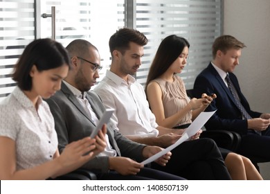 Focused multicultural business people applicants prepare for job interview sit in row line queue, diverse unemployed vacancy seekers group waiting for their turn in office room human resource concept
