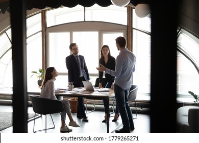 Focused multiethnic employees gather in boardroom talk consider startup plan working on laptop together, concentrated diverse colleagues brainstorm cooperate at office meeting, collaboration concept