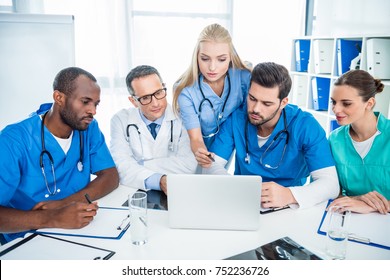 focused multiethnic team of doctors brainstorming and using laptop