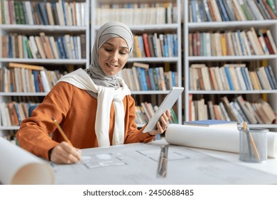 A focused Muslim woman architect, dressed in a hijab, reviews digital blueprints on a tablet while working with physical drafts in a well-stocked library. - Powered by Shutterstock