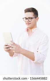 Focused Nerdy Guy In Eyeglasses Reading Or Watching Content On Tablet Screen. Young Man In Glasses Standing Isolated Over White Background. Wi-fi Concept