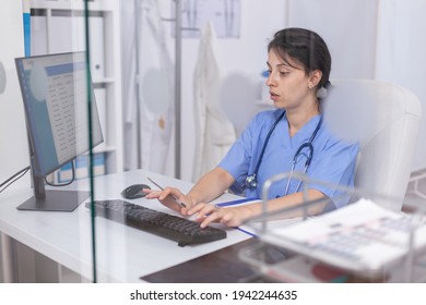 Focused nurse in blue coat checking appointments using computer for healthcare services treatment. Pediatrician assistant specialist in medicine providing professional healtcare services
