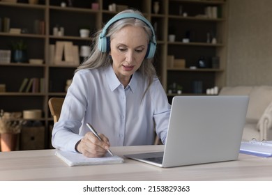 Focused Older Student In Wireless Headphones Watching Virtual Workshop, Learning Webinar On Laptop Computer, Writing Notes, Getting Knowledge, New Profession, Studying Online From Home