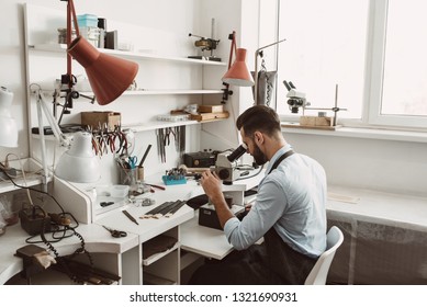 Focused on his job. Side view of a male jeweler looking at the ring through microscope in a workshop. - Powered by Shutterstock