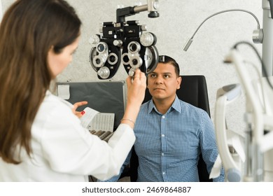 Focused ophthalmologist using a phoropter while examining the eyesight of a male patient in a modern optometry clinic setting - Powered by Shutterstock