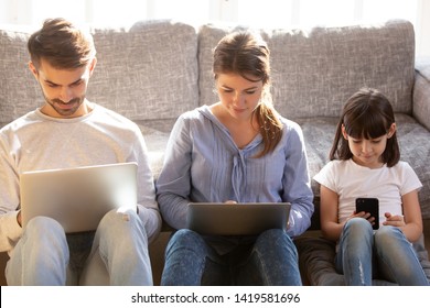 Focused Parents And Preschooler Kid Sit In Living Room Using Electronic Devices Not Talking, Modern Young Family With Little Daughter Work On Gadgets, Play Or Surf Internet Relaxing At Home