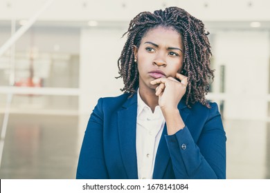 Focused Pensive Leader Thinking Outside. Serious Young Black Business Woman Standing At Outdoor Glass Wall, Touching Chin And Looking Away Into Distance. Thinking Concept