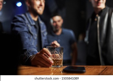 Focused Photo. Friends In The Bar. Man Holds Glass With Whiskey.