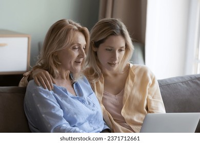 Focused positive mature mother and beautiful young grownup daughter using online ecommerce app on laptop, watching movie, interactive TV channel, enjoying domestic wireless connection, communication - Powered by Shutterstock