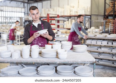 Focused pottery expert in maroon apron meticulously inspecting quality of freshly produced handmade plate in artisanal ceramics studio - Powered by Shutterstock