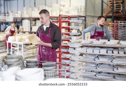 Focused pottery expert in maroon apron meticulously inspecting quality of freshly produced handmade plate in artisanal ceramics studio - Powered by Shutterstock