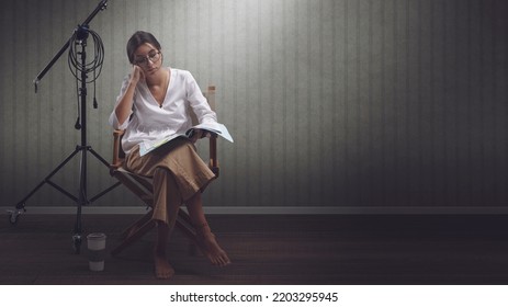 Focused Professional Actress Sitting On The Director's Chair And Reading A Play Script, Blank Copy Space