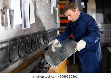 Focused professional craftsman in metalworking shop operating press brake, carefully positioning metal workpiece for bending on machine - Powered by Shutterstock