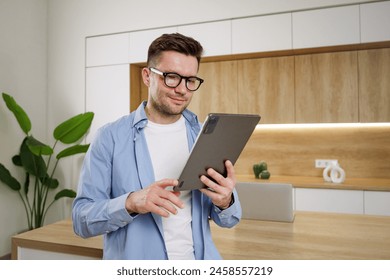 A focused professional in glasses holding a tablet, standing in a modern office with wooden and green plant accents.

 - Powered by Shutterstock