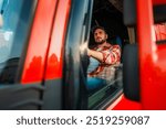 Focused professional truck driver driving a red truck, he is wearing casual clothes with a blue hat.