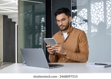 Focused professional using a tablet while working in a modern office setting. Man is engaged and appears to be concentrated. - Powered by Shutterstock