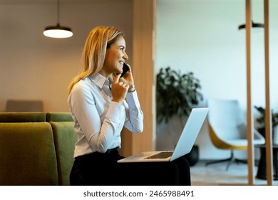 Focused professional woman multitasks efficiently, speaking on the phone and typing on her laptop in a bright, contemporary office space - Powered by Shutterstock