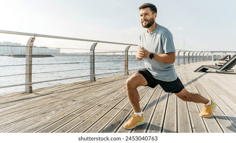 A focused runner performs lunges on a waterfront boardwalk, with a serene river and bridge under a wide sky in the background.