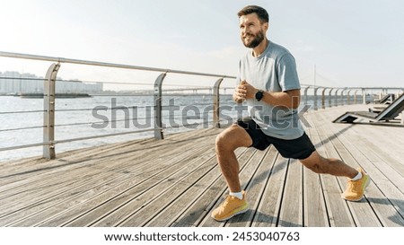 A focused runner performs lunges on a waterfront boardwalk, with a serene river and bridge under a wide sky in the background.