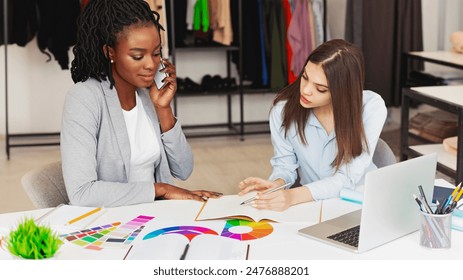 A focused scene unfolds with two professional multiracial women working closely together at a white table filled with vibrant color samples. - Powered by Shutterstock