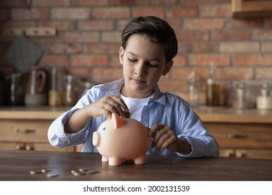 Focused school kid saving money for purchase, putting cash in pink piggy bank at home. Preschooler child learning to calculate personal budget, manage finance, playing investment, accounting - Powered by Shutterstock