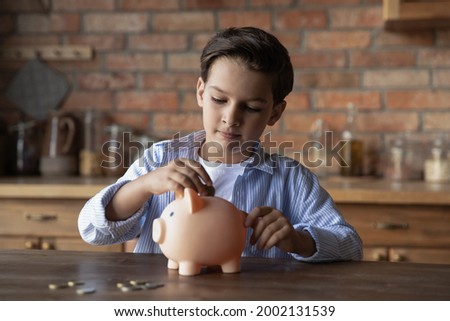 Focused school kid saving money for purchase, putting cash in pink piggy bank at home. Preschooler child learning to calculate personal budget, manage finance, playing investment, accounting