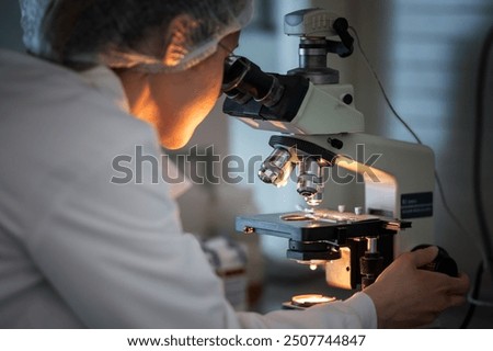 A focused scientist peers into a microscope, meticulously analyzing samples in a dimly lit lab, highlighting the precision and dedication involved in scientific research
