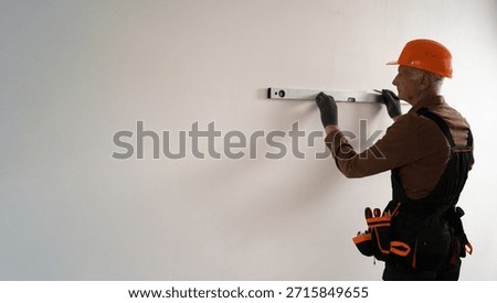 Focused Senior elderly builder using spirit level for measuring wall and making marks during building construction or renovation. construction professional at work. copy space
