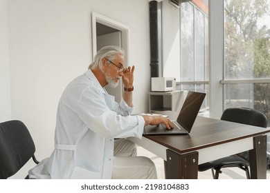 Focused Senior Healthcare Worker In Glasses Using Laptop While Working At Doctor's Office