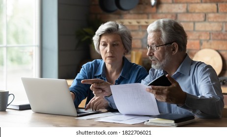 Focused senior husband and wife sit at table at home look at laptop screen pay bills taxes online. Concentrated mature man and woman couple make internet payment on computer, manage finances - Shutterstock ID 1822706021