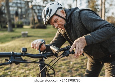 A focused senior man wearing a helmet is adjusting the handlebars on his mountain bike, preparing for a ride through a park. - Powered by Shutterstock