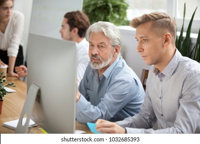 Focused Senior And Young Colleagues Discussing Online Project Looking At Pc Screen, Older Mentor Helps Employee Explaining Computer Task, Team Coworkers Talking Working Together, Corporate Teamwork