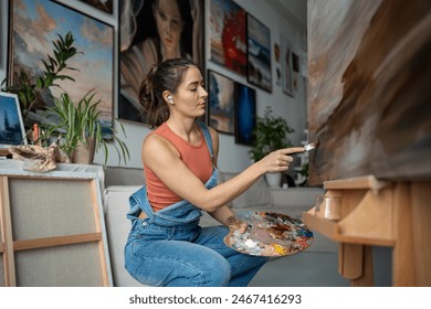 Focused serious woman artist working on abstract painting with careful gentle strokes of small brush. Girl wear earphones creating dark impressionistic picture expressing melancholic lyrical feelings - Powered by Shutterstock