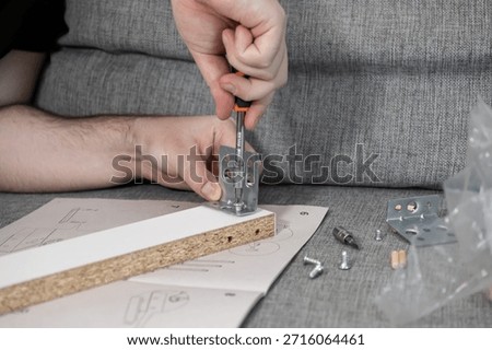 A focused shot of hands carefully assembling flat-pack furniture with a screwdriver, showcasing the process of home improvement, manual work, and self-reliance
