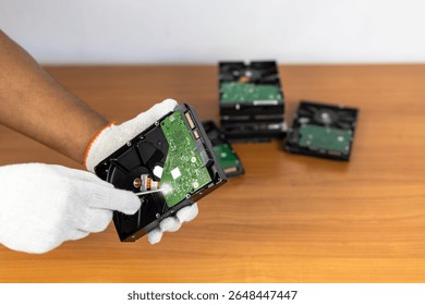 A focused shot on a person wearing white protective gloves, performing intricate work on a hard drive with a screwdriver. The circuit board of the hard drive emits a subtle glow