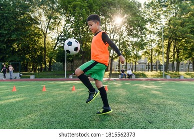 Focused skillful teen football player stuffs soccer ball on leg. Practicing sport exercises at artificial stadium.